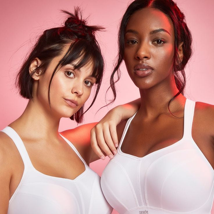 Two women wearing white sports bras against a pink background.